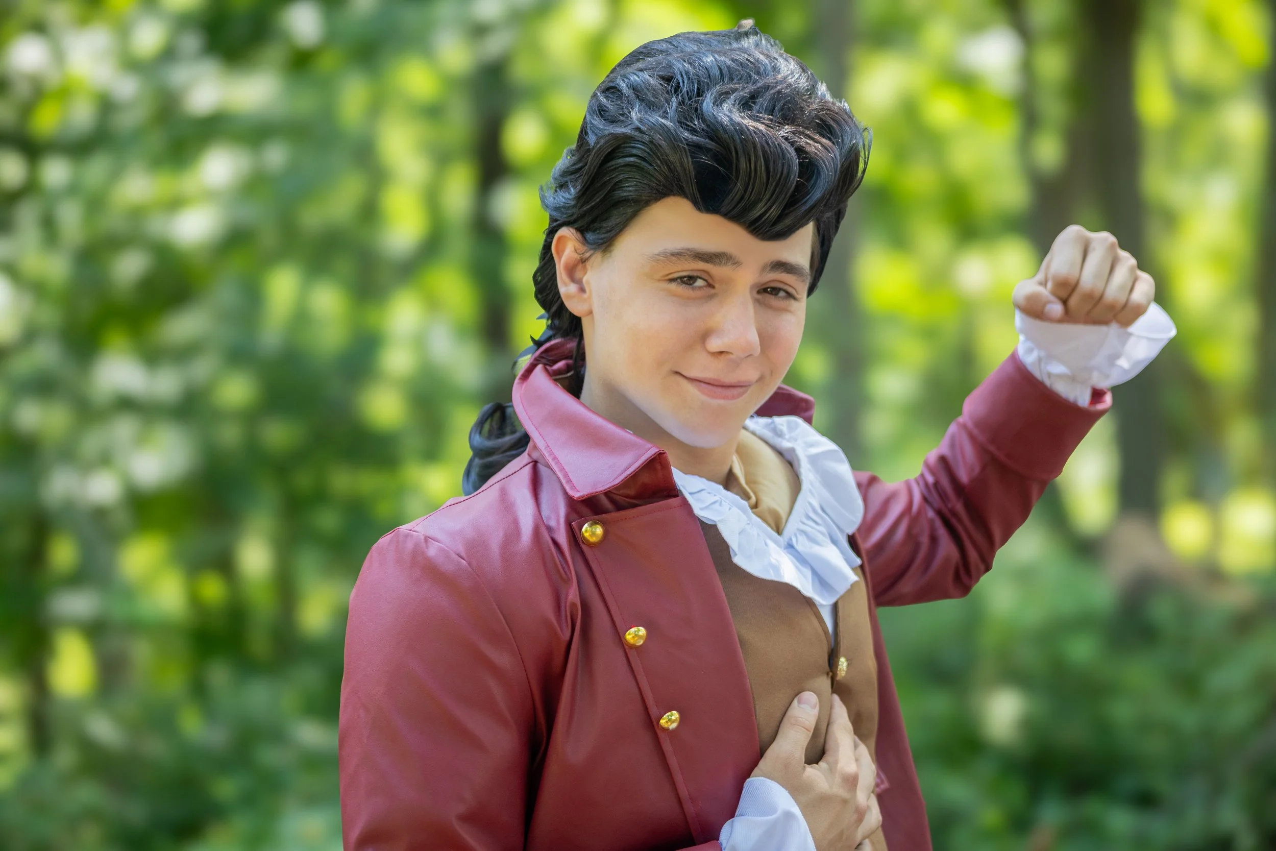 A person dressed as Gaston from Beauty and the Beast, standing outdoors in front of a blurry green forest.