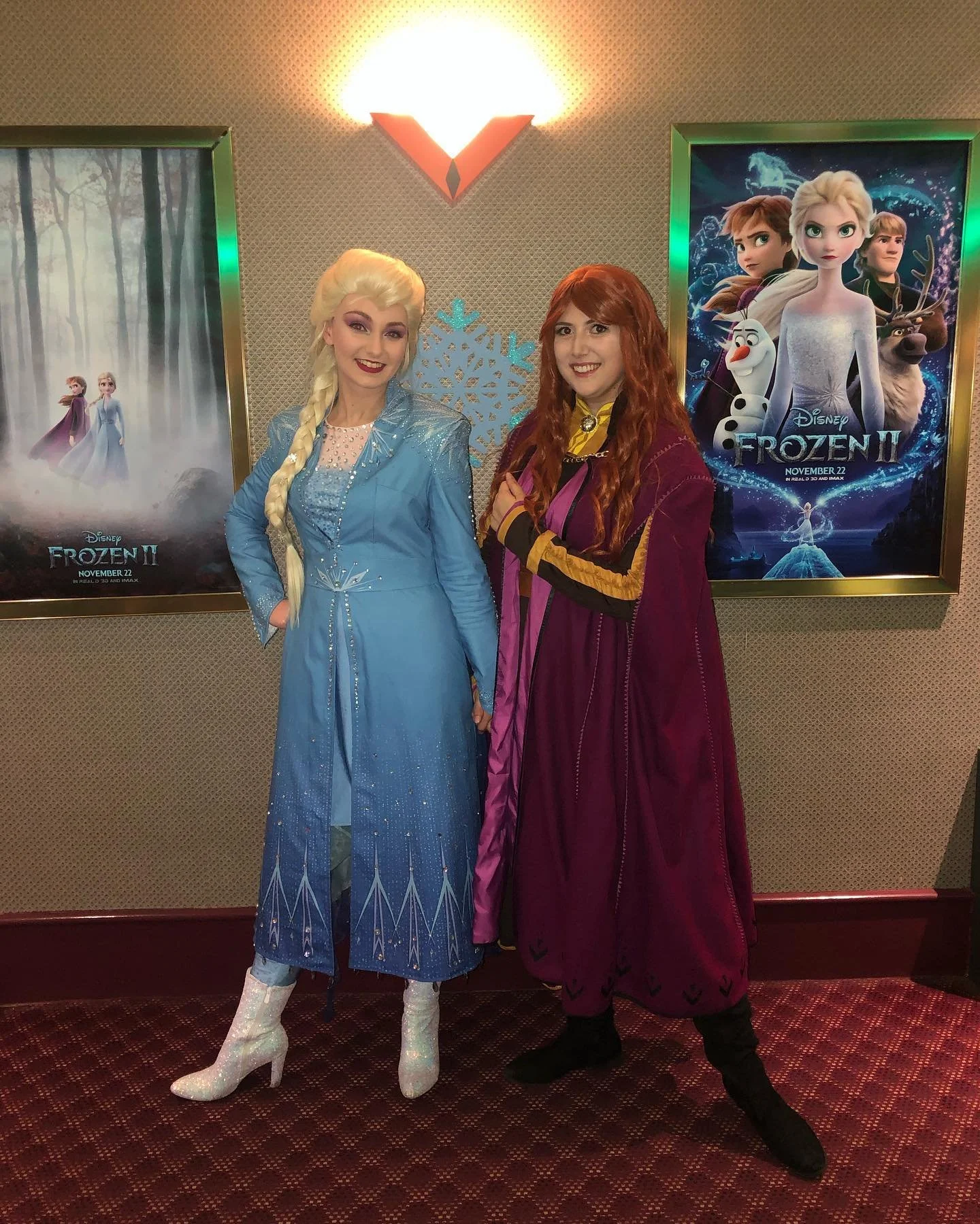Two women dressed as Elsa and Anna from Frozen standing in front of movie posters for Disney's Frozen II.