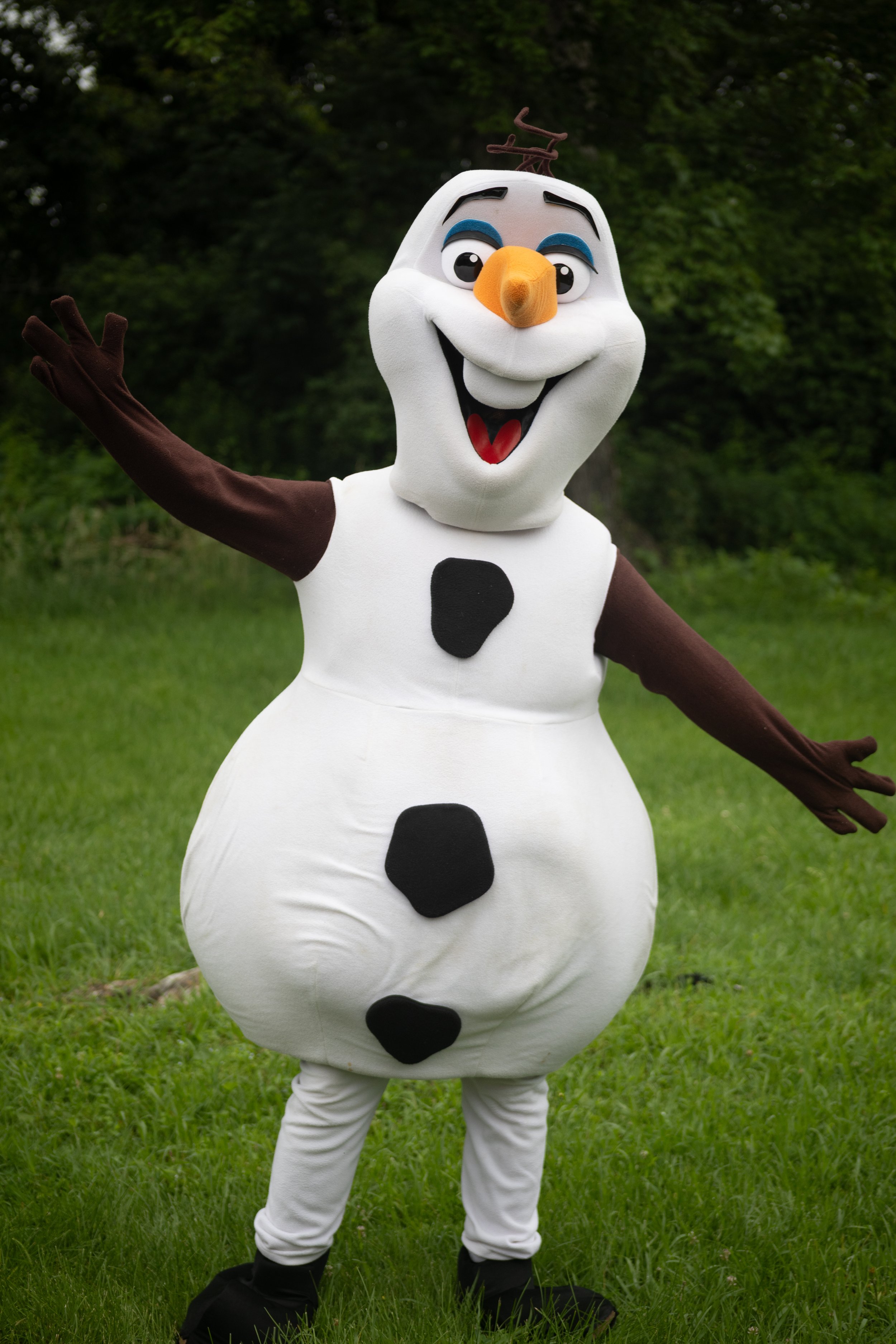 Person dressed in a snowman costume with a wide smile, standing outdoors on grass with trees in the background, inspired by Olaf from Frozen.