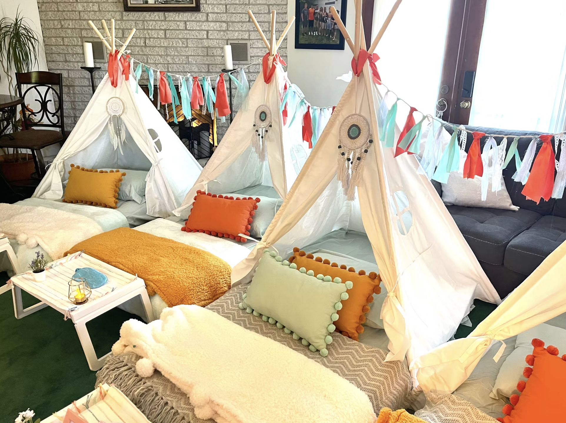 Indoor party setup with miniature tents decorated with dreamcatchers and colorful bunting, placed on a cozy floor seating area with pillows and blankets.
