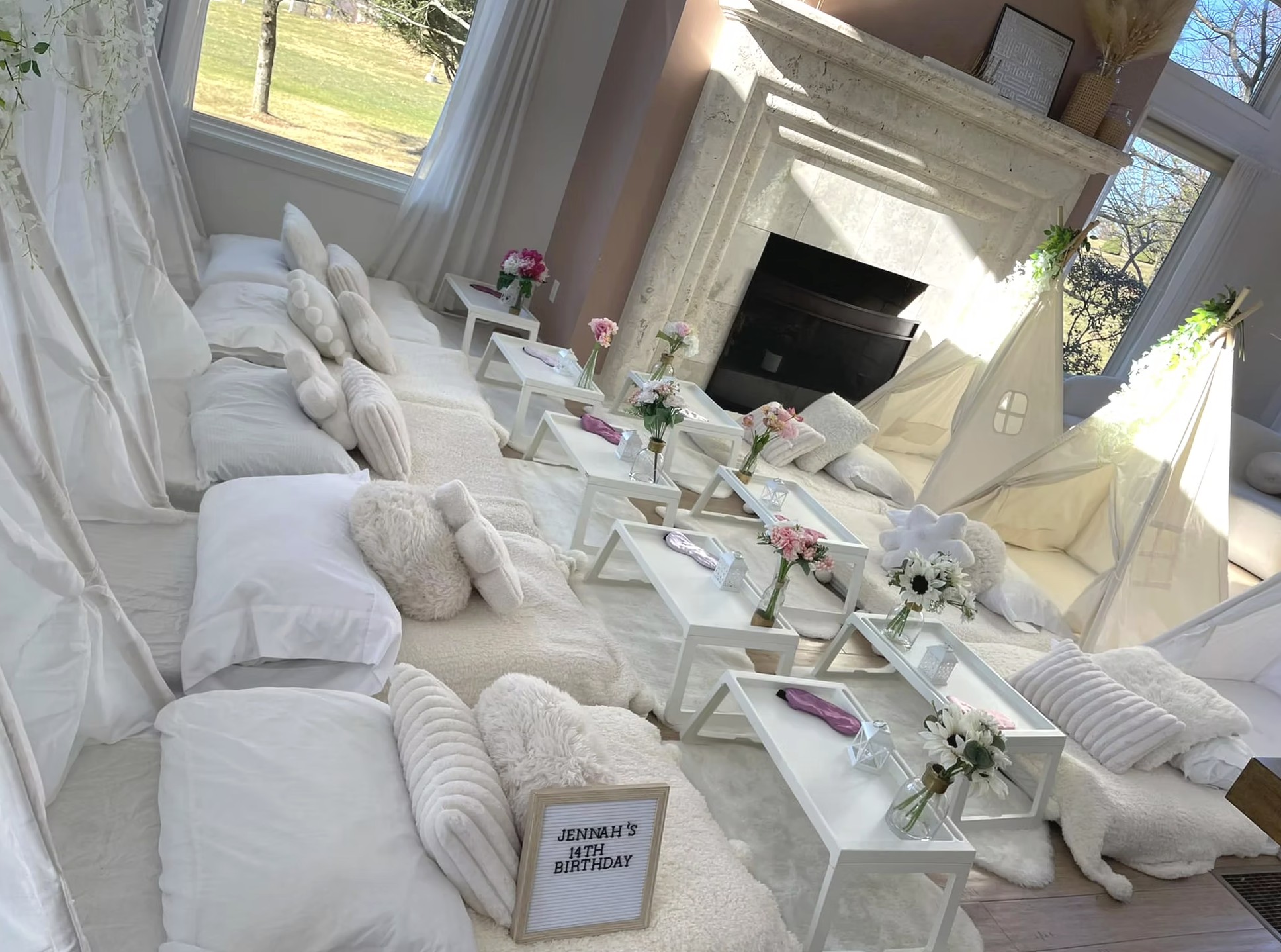 Cozy indoor space decorated for a girl's 14th birthday party with white and pastel decor, fur rugs, plush pillows, and small tables with flowers and party favors.