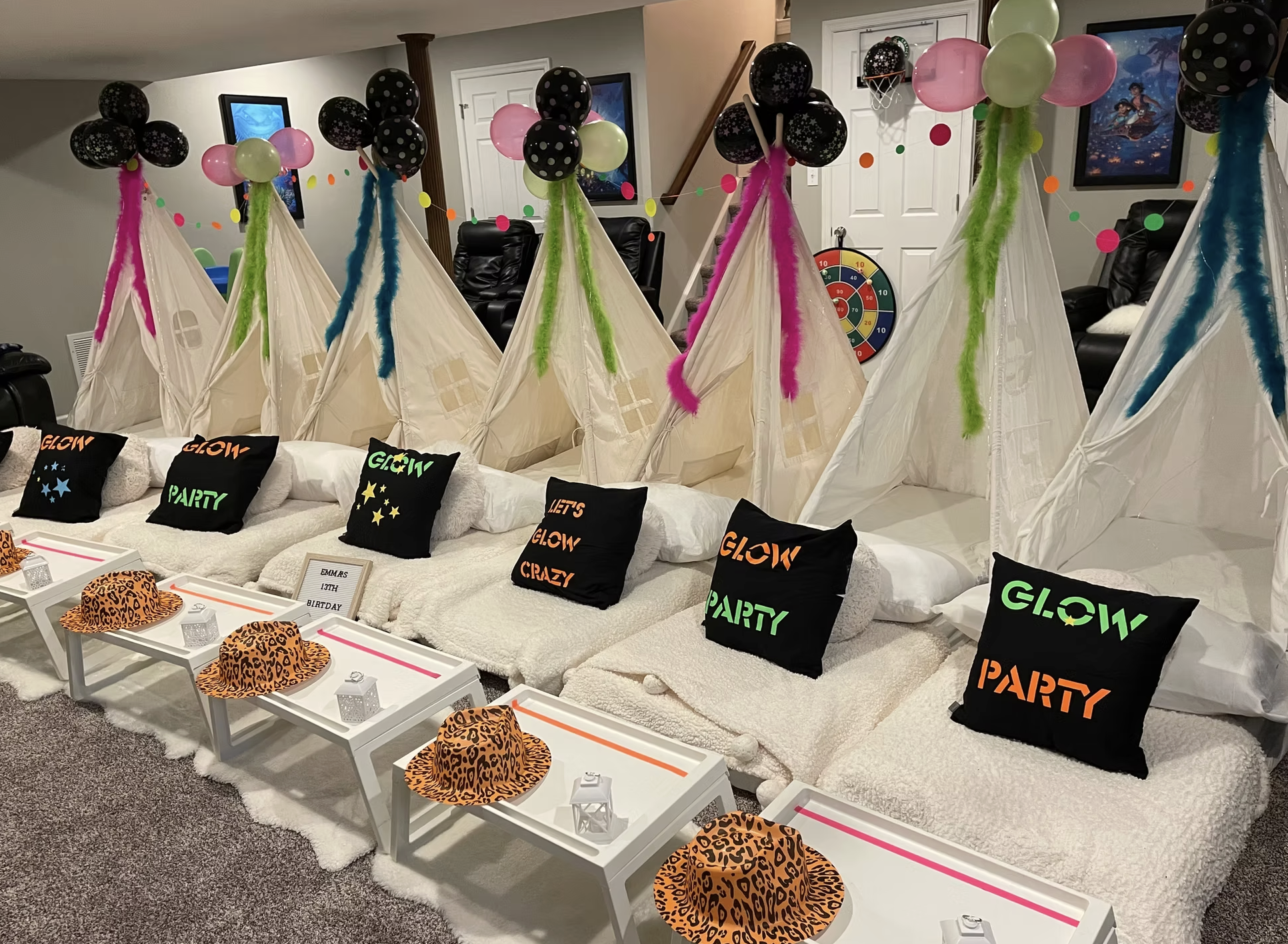 Indoor birthday party setup featuring six teepee tents decorated with colorful balloons and streamers, each with a pillow reading 'Glow Party' or 'Let's Glow Crazy,' with small white tables, orange leopard print hats, and small decorative lanterns in