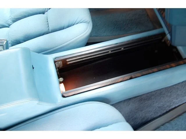 Open center console in a light blue car showing empty storage compartment.