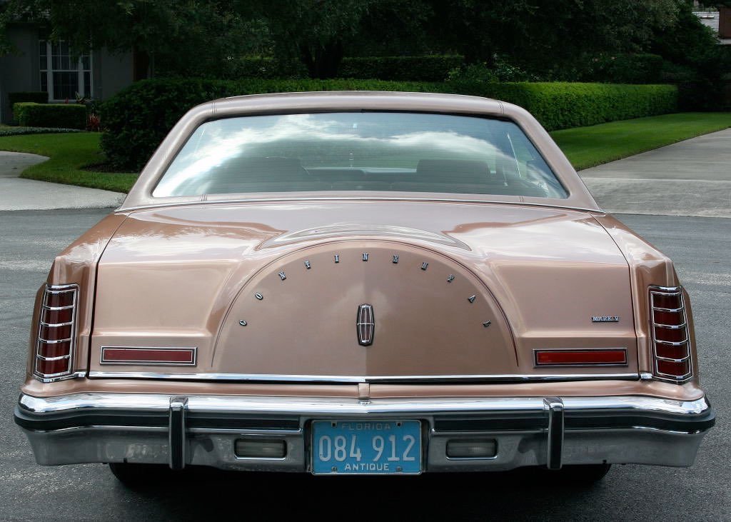 Rear view of a vintage beige Lincolnia car with a spare tire cover, Florida license plate, and classic taillights parked on a suburban street.