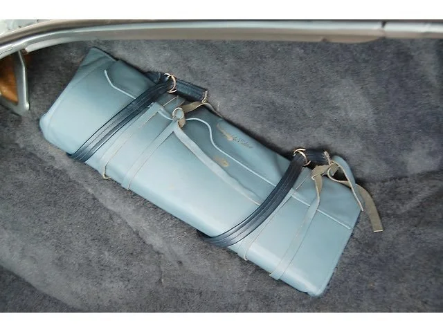 A blue golf club carry bag lying on a gray car floor mat.