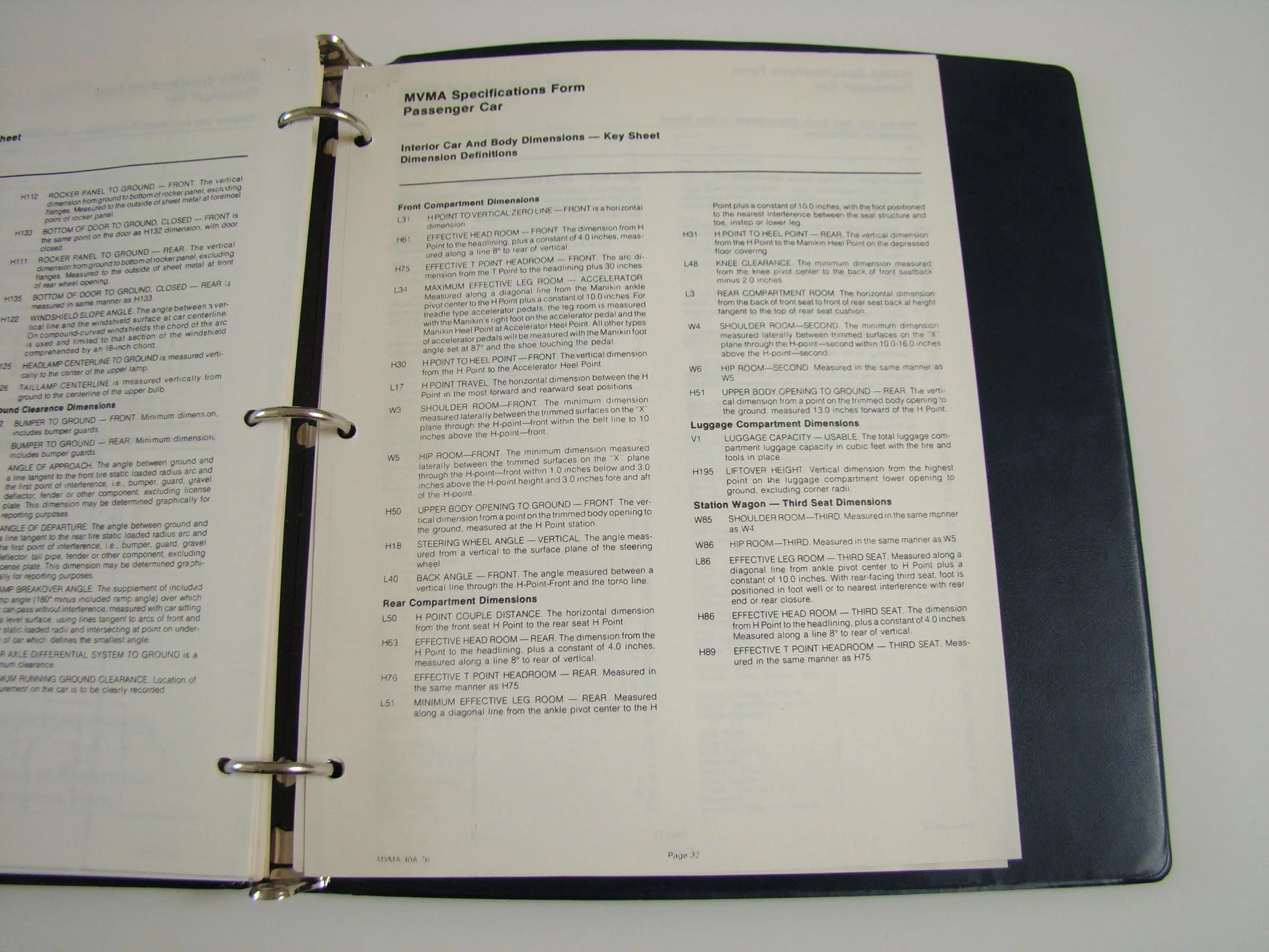 Open binder containing a printed specifications form for a passenger car, with various technical details and measurements listed on the page.