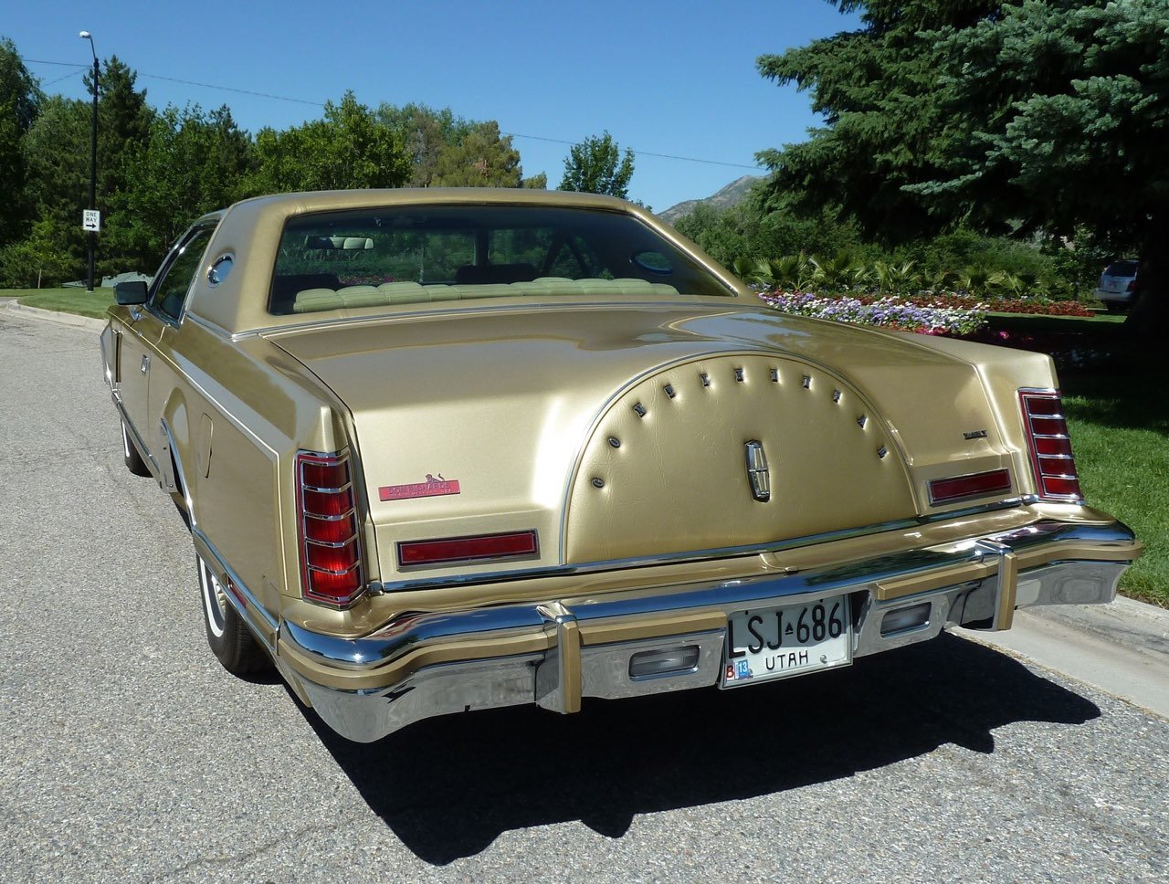 A vintage gold-colored Lincoln Continental car parked on a street with green trees and mountains in the background.