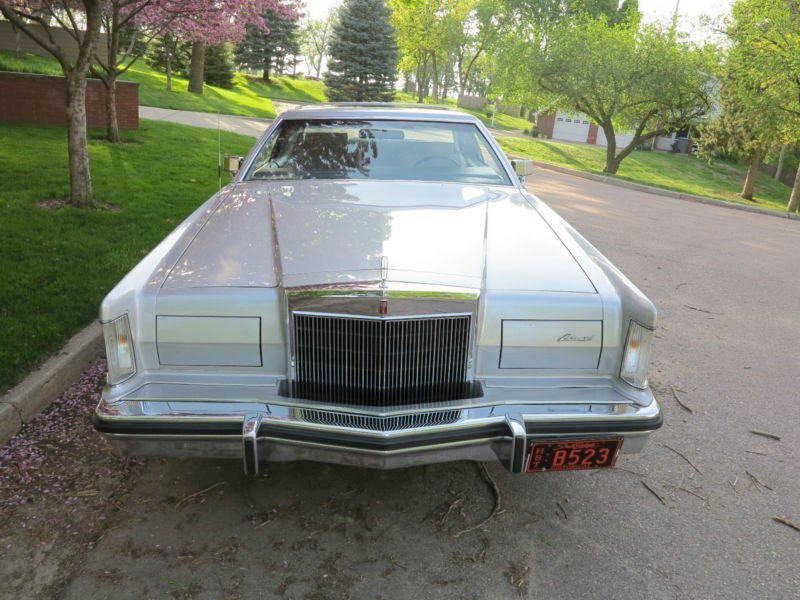 A classic white Cadillac parked on a suburban street with green trees and grass in the background.