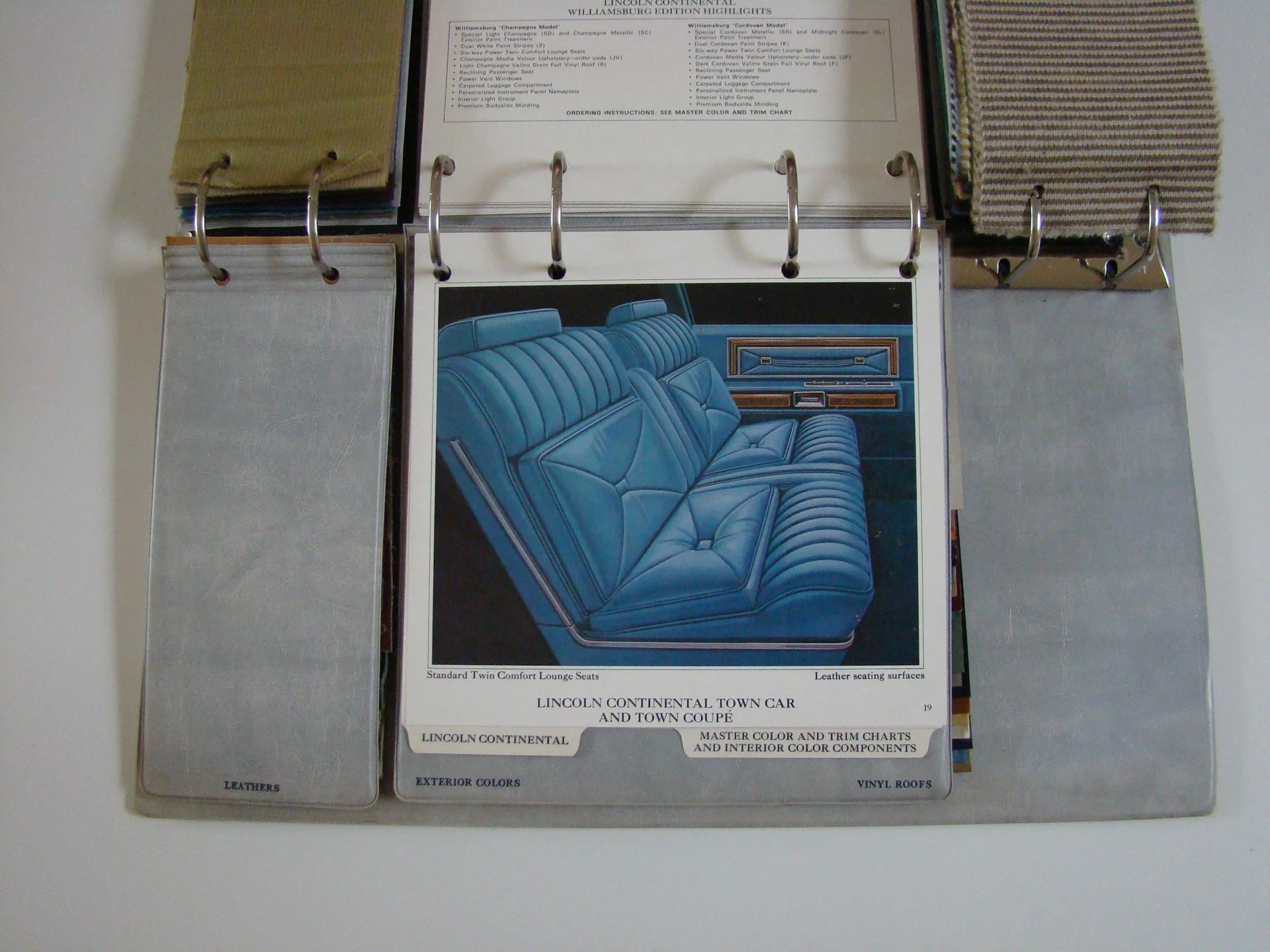 Open sample book features fabric and leather swatches, paint and color samples, mainly for car interior with a focus on Lincoln Continental models. The visible page displays a color illustration of a blue leather car interior seating.