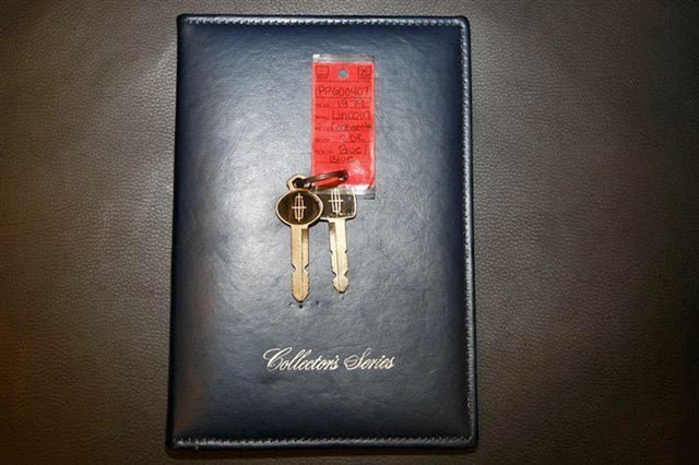 A black leather-bound journal labeled "Collector's Series" with two car keys attached to a red key tag on top of the journal.