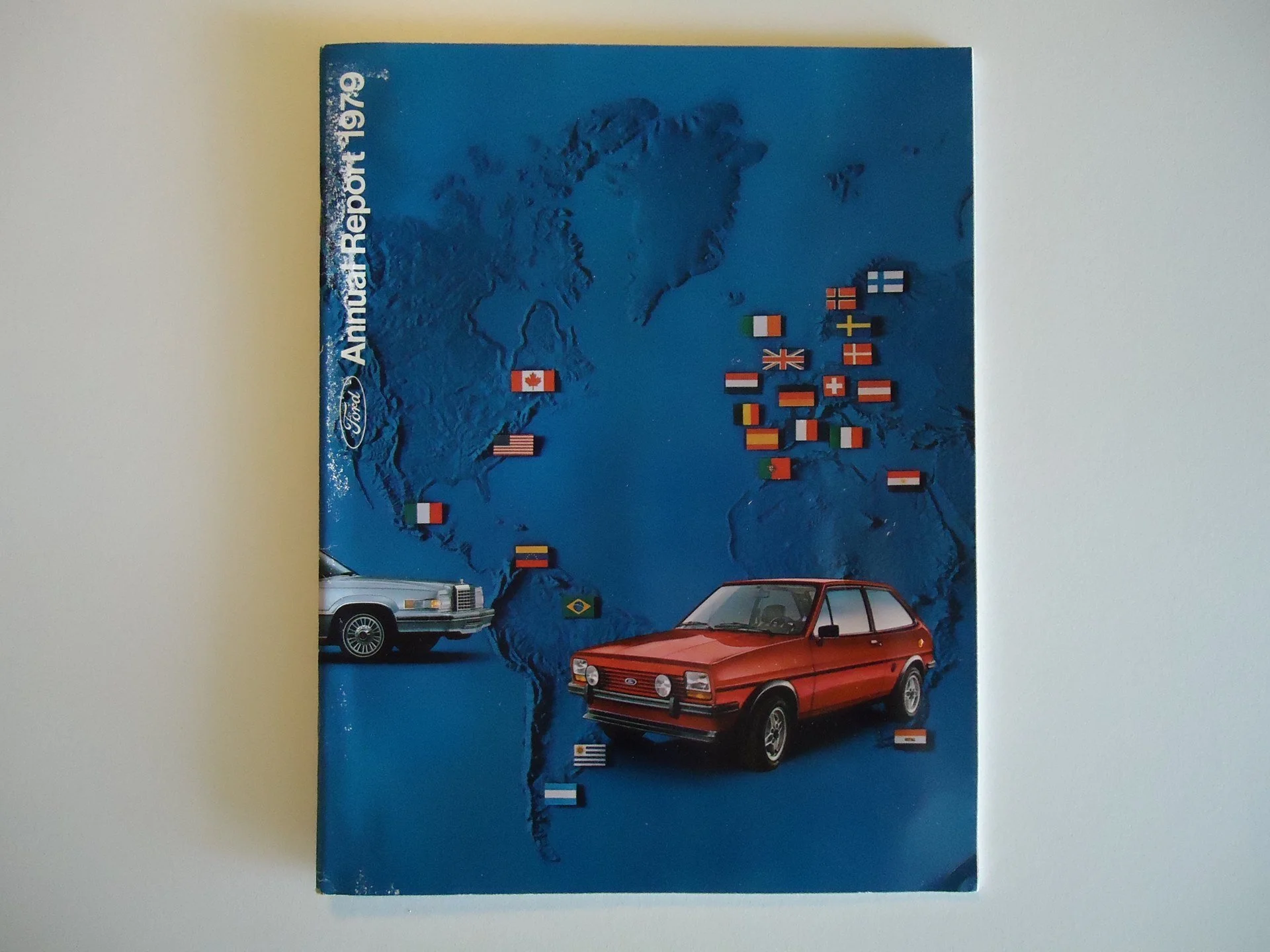 Ford annual report cover from 1979 featuring a map of the world, multiple country flags, and two vintage cars, one red and one white.