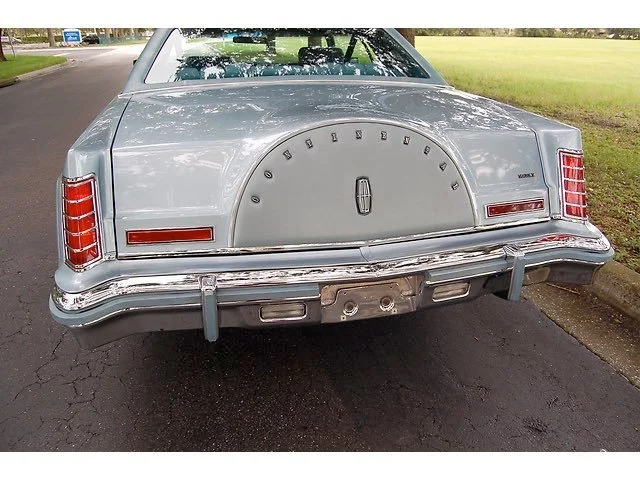 Rear view of a vintage Lincoln Continental with a spare tire cover on the trunk, parked on a suburban street.