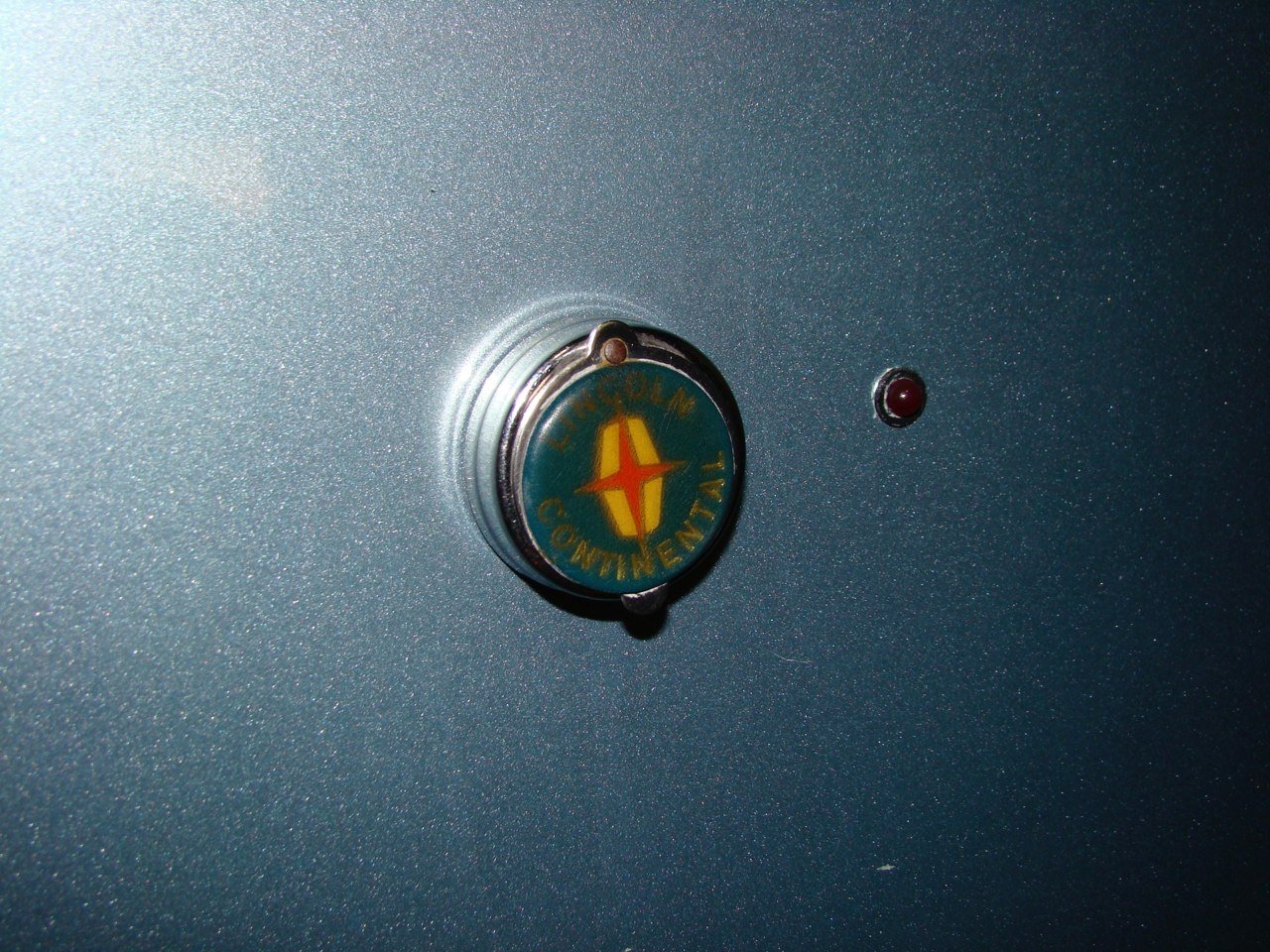 A close-up of the TOLM Continentail badge mounted on a light blue surface with a small red indicator light nearby.