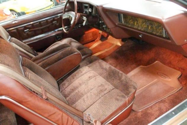 Interior of a vintage car with brown fabric and leather seats, steering wheel, dashboard with radio, and passenger side floor mat.