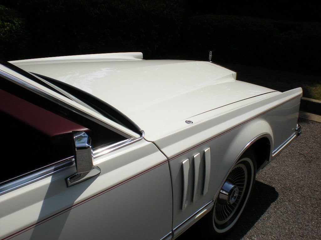 Close-up of a vintage white car with chrome accents, parked on asphalt with a grassy area in the background.