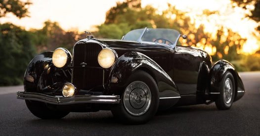 Black vintage convertible car parked on the road at sunset.