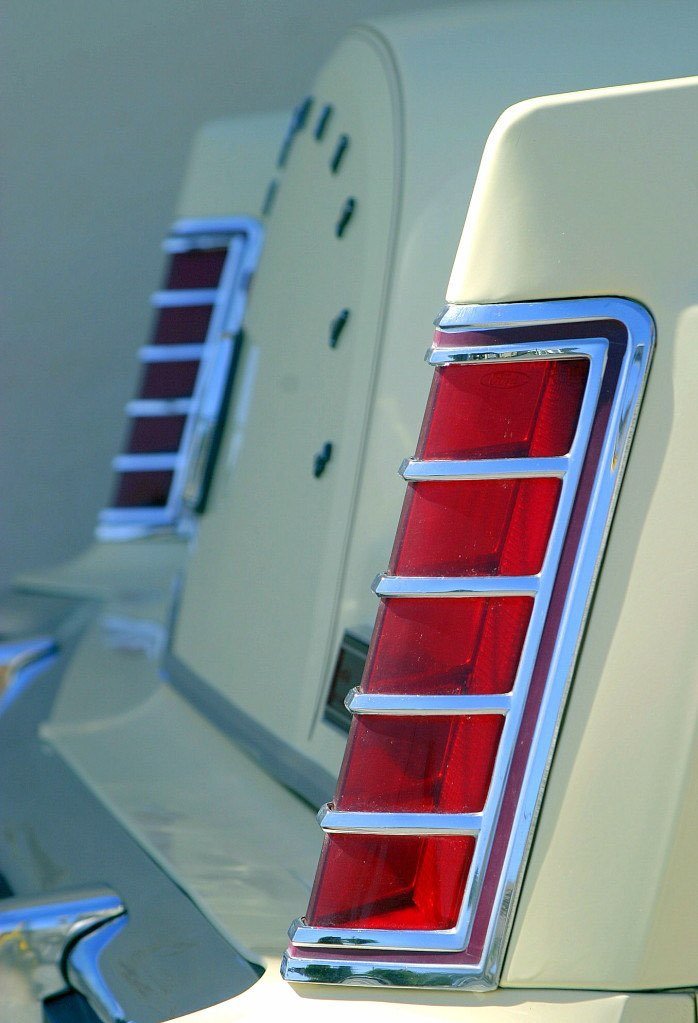 Close-up of the tail light of a vintage car, showing red sections and chrome details.