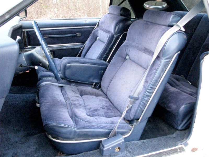 Interior of a vintage car showing two front seats, a dashboard, and a rear bench seat, all with plush fabric upholstery.