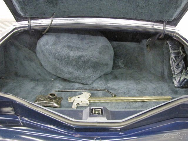 The trunk of a car containing a large gray bag, a black object, and some metal rods or tools.