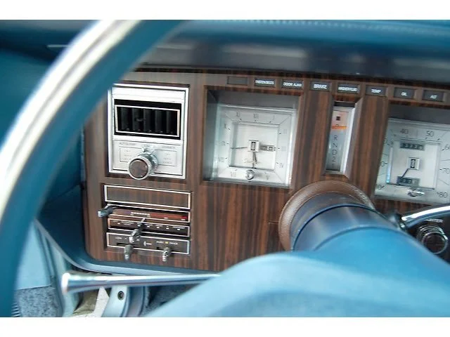 Close-up of a vintage car dashboard with wood grain panel, featuring an analog clock, radio, and speedometer.