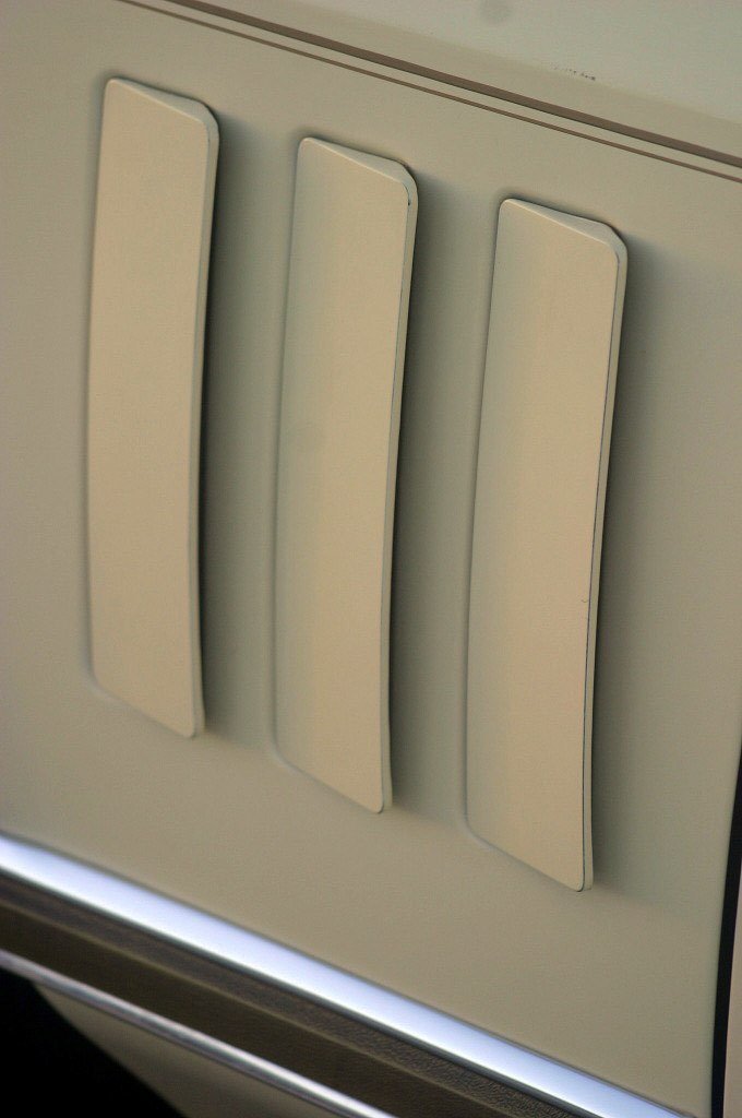 Close-up of an air conditioning unit or heater vent with three vertical, cream-colored louvers.