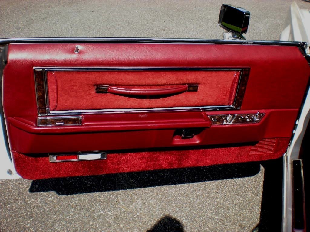 Close-up of a vintage car door interior with red upholstery, chrome accents, and a black handle, viewed from above.