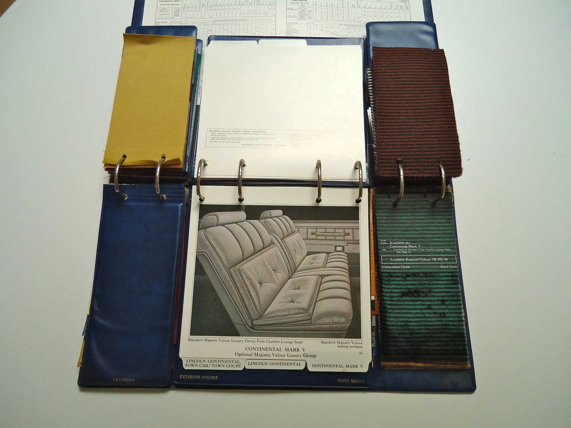 Automotive interior sample book showing fabric swatches, color options, and a brochure of a leather couch for a Lincoln Continental vehicle.