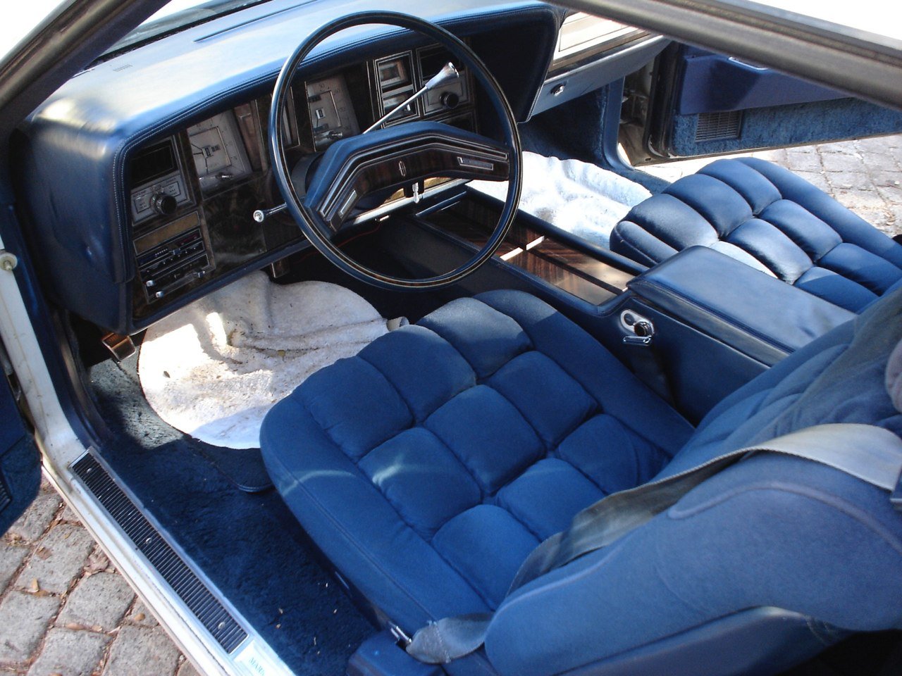 Interior of a vintage car with blue velvet seats, a dashboard with multiple gauges, and a large steering wheel.