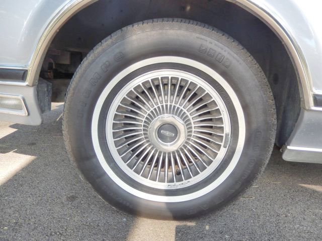 Close-up of a car wheel with a silver hubcap and whitewall tire on asphalt pavement.