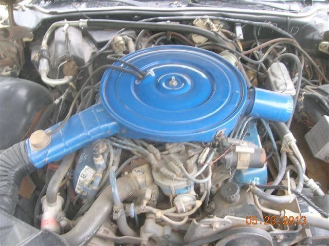 Car engine with blue air cleaner and hoses, various wires and components.