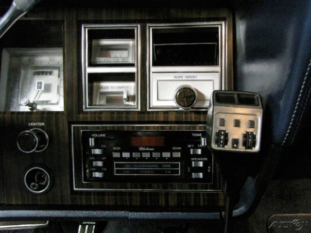 Dashboard of a vintage car with an analog radio, switches for lights, and a small device attached to the right.