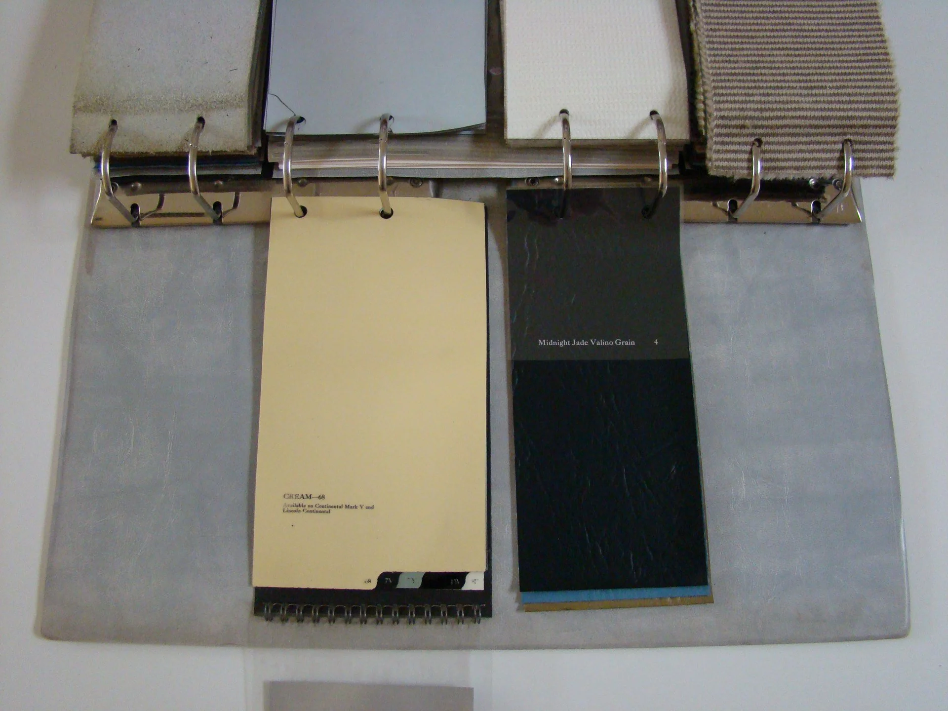 Swatch color samples attached to a color display book, including shades of cream and black with name labels, on a metal surface.