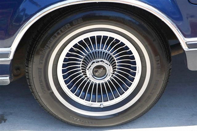 Close-up of a classic car wheel with a white wire spoke rim and a black tire.