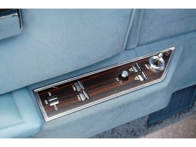 Car seatback with a woodgrain control panel featuring switches and a joystick for seat adjustments.