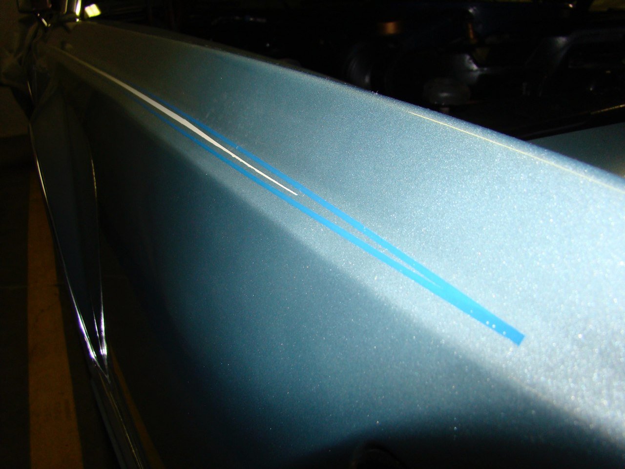 Close-up of a metallic blue car door with a blue stripe detail.