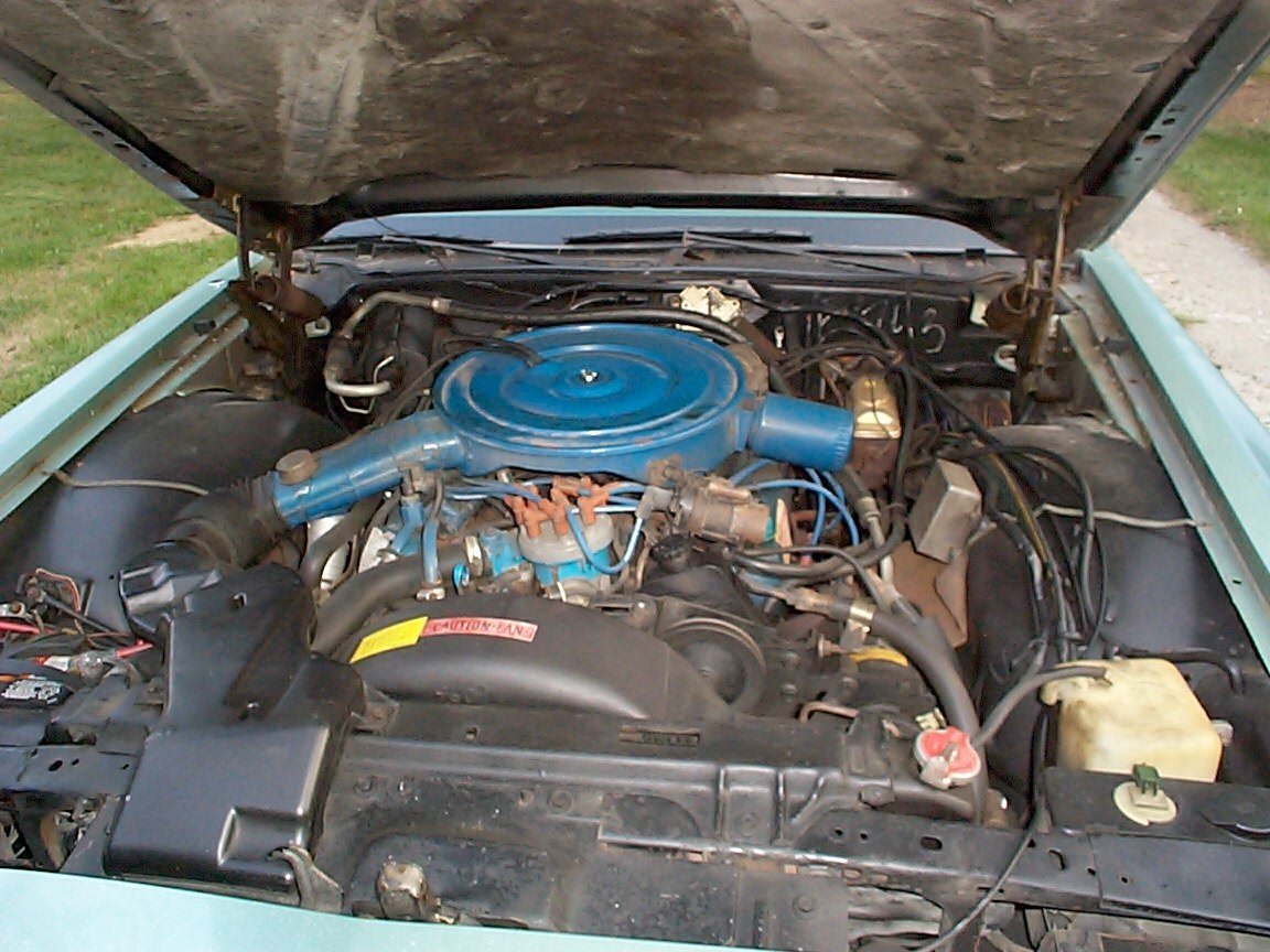 Open hood of a vintage blue car showing the engine bay with a blue air filter housing and various engine components.