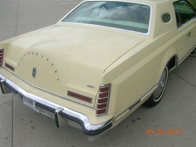 A vintage cream-colored sedan with a unique speedometer design on the trunk and a classic chrome bumper.
