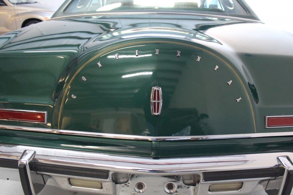 Rear view of a classic green Oldsmobile car with chrome bumper and Lincoln emblem on trunk.