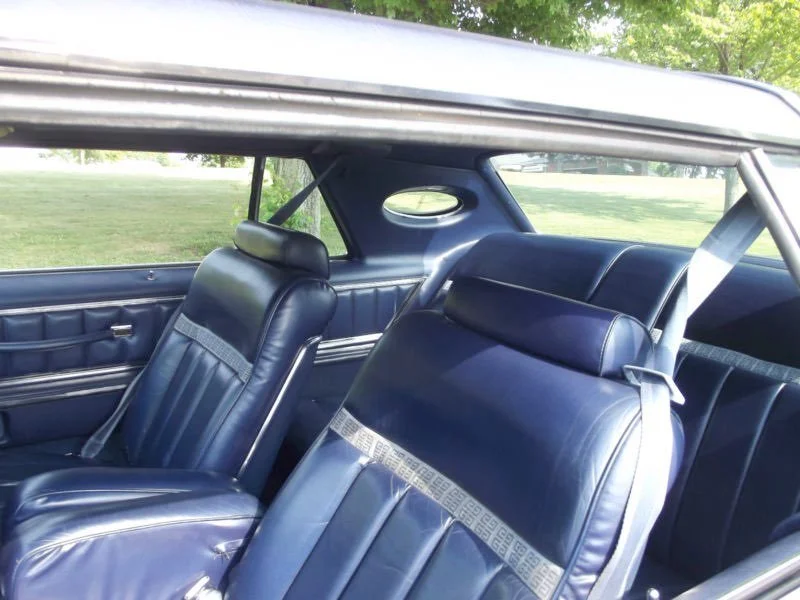 Interior of a vintage car featuring blue leather seats and a side window.