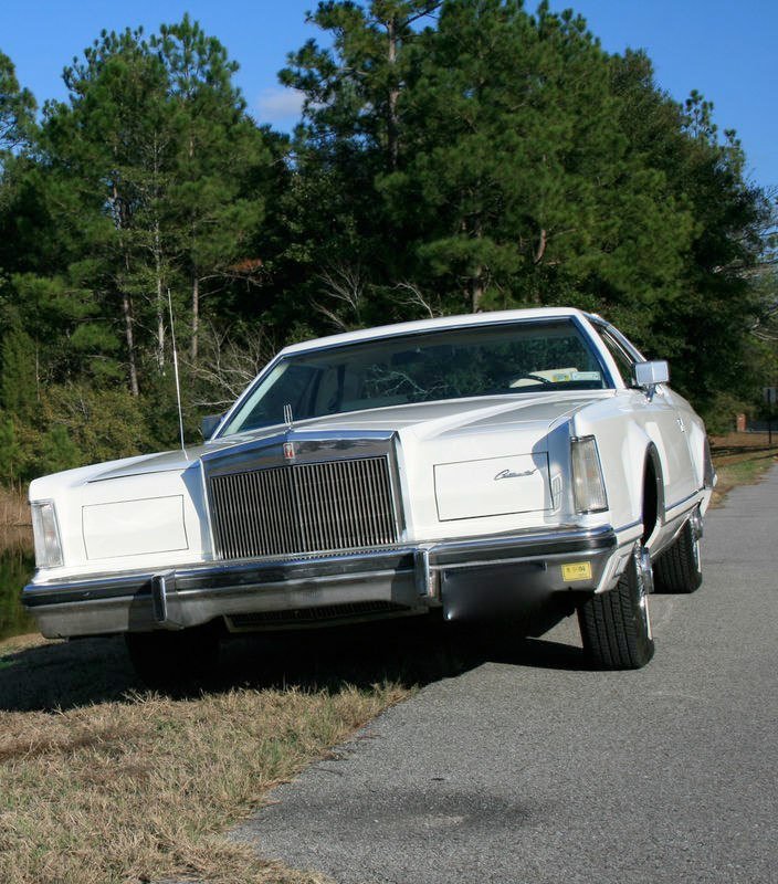 A classic white Cadillac parked on the side of a road with trees in the background.