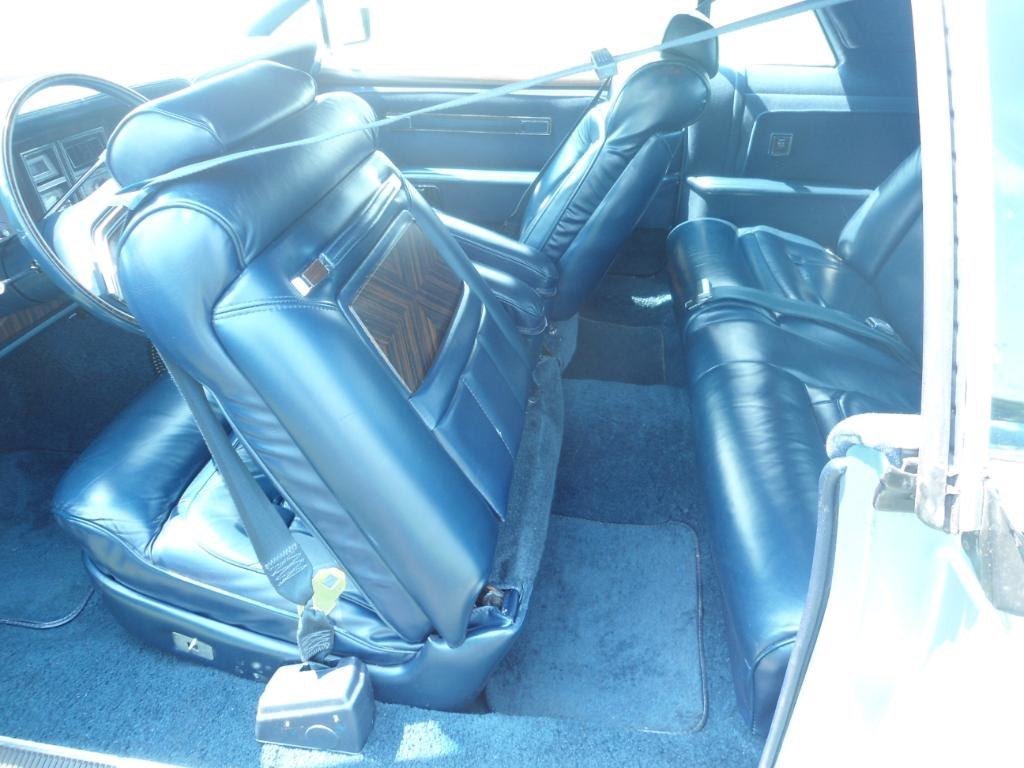 The interior of a vintage vehicle with blue leather seats, including a front bench seat and a back seat, and a steering wheel visible.