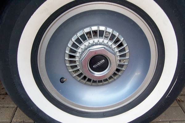 Close-up of a vintage car wheel with a hubcap and whitewall tire.