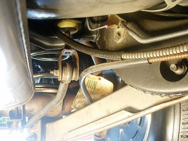 Close-up view of a car's engine compartment showing various metal and rubber hoses, a wheel lug nut, and a yellow component with writing on it.