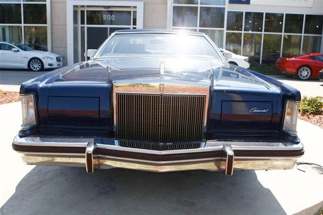 Front view of a vintage black Cadillac vehicle parked outdoors in front of a building with large windows.