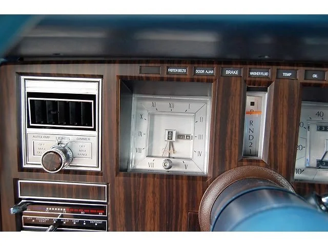 Close-up of a classic car dashboard with a wood grain finish, featuring a clock, various switches, and gauges.