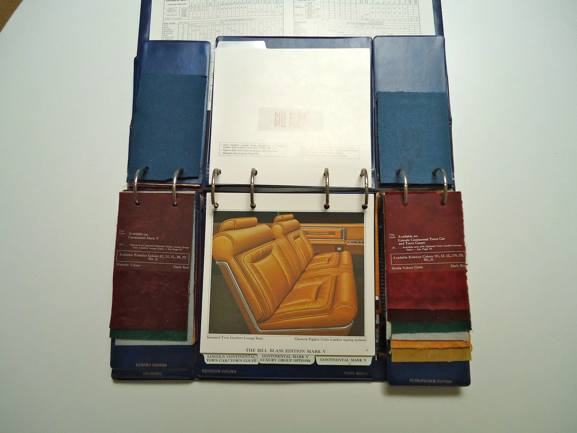 A sample book or color swatch binder open to display material samples, including fabric and leather, with a sample of yellow car interior upholstery in the center.