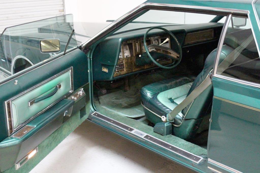 Interior of a vintage car with green upholstery, steering wheel, dashboard, and front seat.