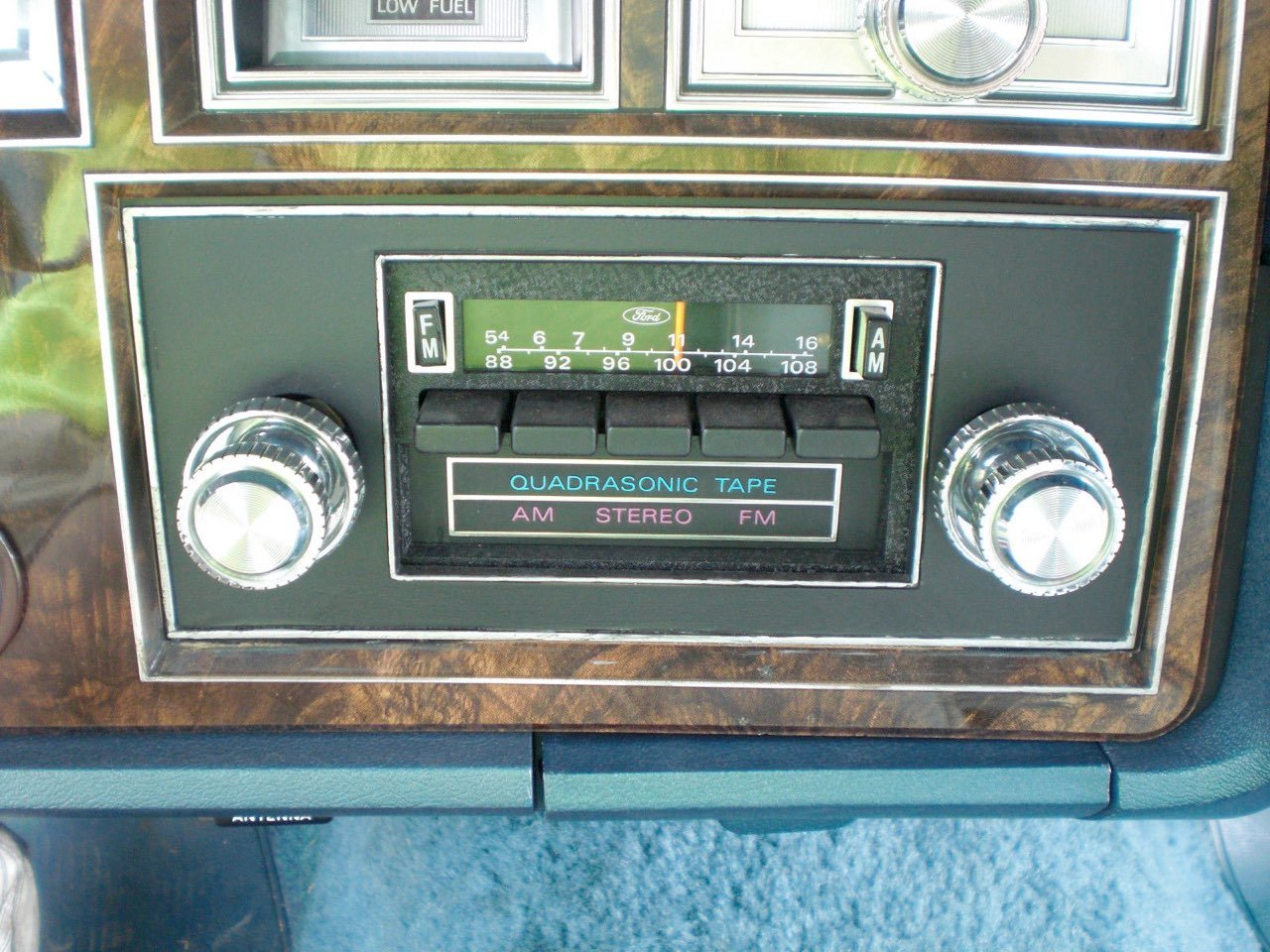 Vintage car radio with woodgrain panel, tuning dial, and buttons for AM, FM, stereo, and quadrasonic tape.