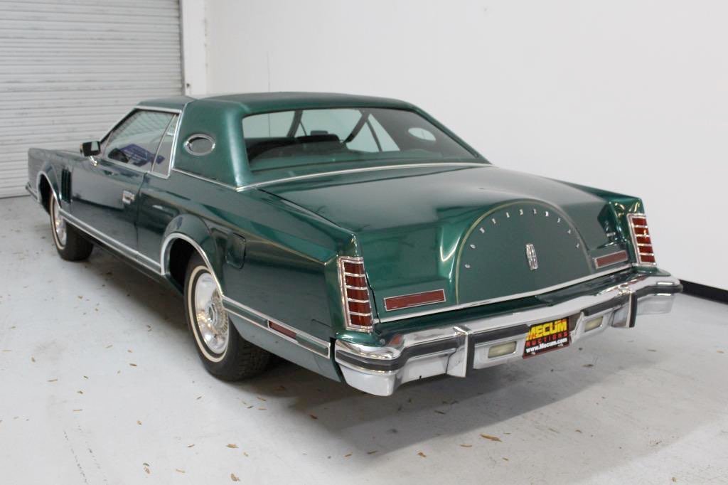 A vintage green luxury car with a hardtop roof, chrome details, and classic design parked indoors.