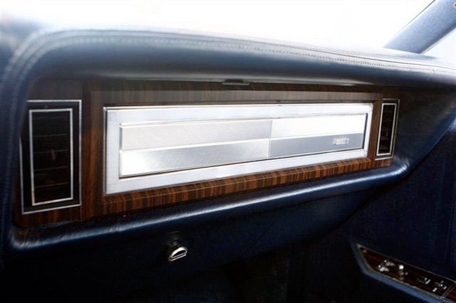 Dashboard of a vintage car with a woodgrain finish and a metal horizontal strip in the center.
